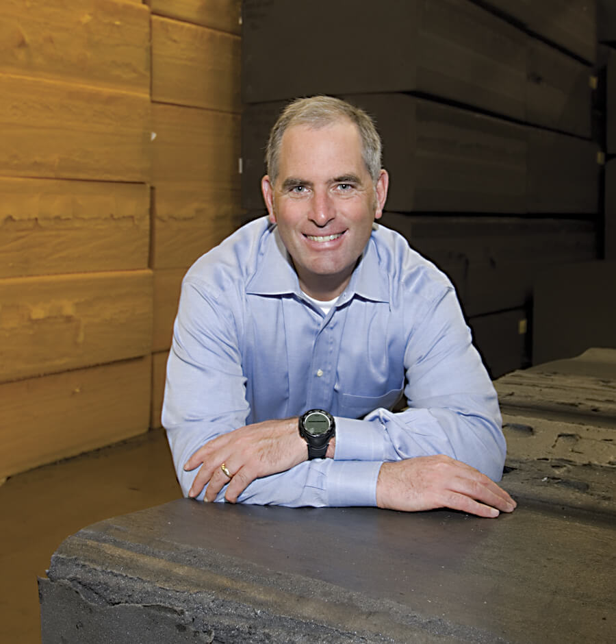 A man leaning on a table in front of wood.